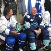 two men in hockey equioment sitting in the changeroom talking