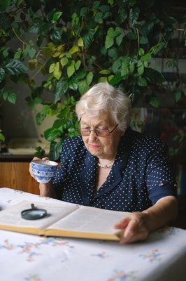 Older woman drinking tea and reading outside