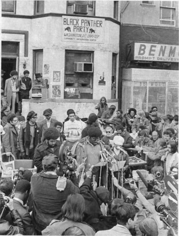Black and white image of Elbert "Big Man" Howard" speaking to the press in a mass of people in the street.