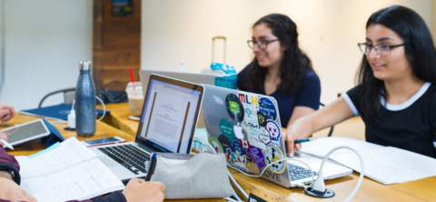 A group of three students seated at a table working on their laptops