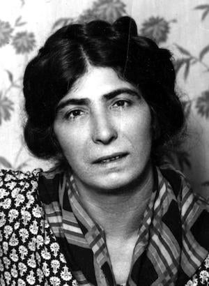 A black and white close up image of a woman, Milly Witkop-Rocker, with dark, styled hair, wearing flannel, looking at the camera.