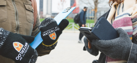 Hands of two students, one is holding a clipboard and the other is holding their phone