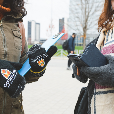The hands of two students, one wearing University of Waterloo gloves, and the other is holding a cell phone