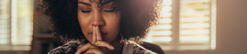 A black woman looking peaceful with her eyes closed and fingers in front of her lips.