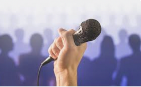 Hand holding a microphone with an audience in the background