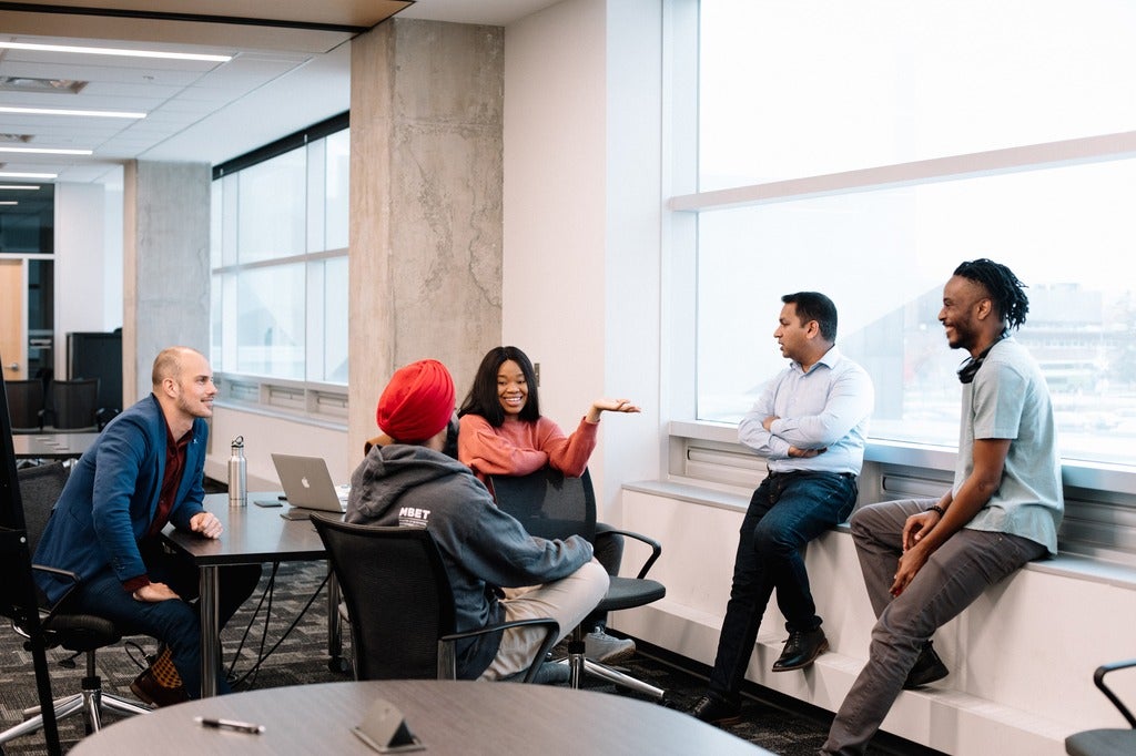 A group of five people smiling and talking in a classroom