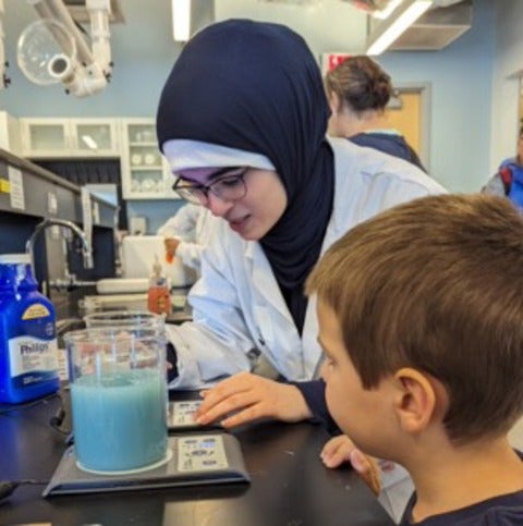 Person in lab coat showing a kid a beaker with a blue liquid inside