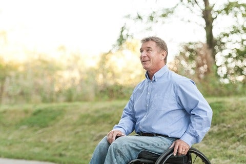 Rick Hansen in dress shirt and jeans sits in wheelchair outside on sunny day.