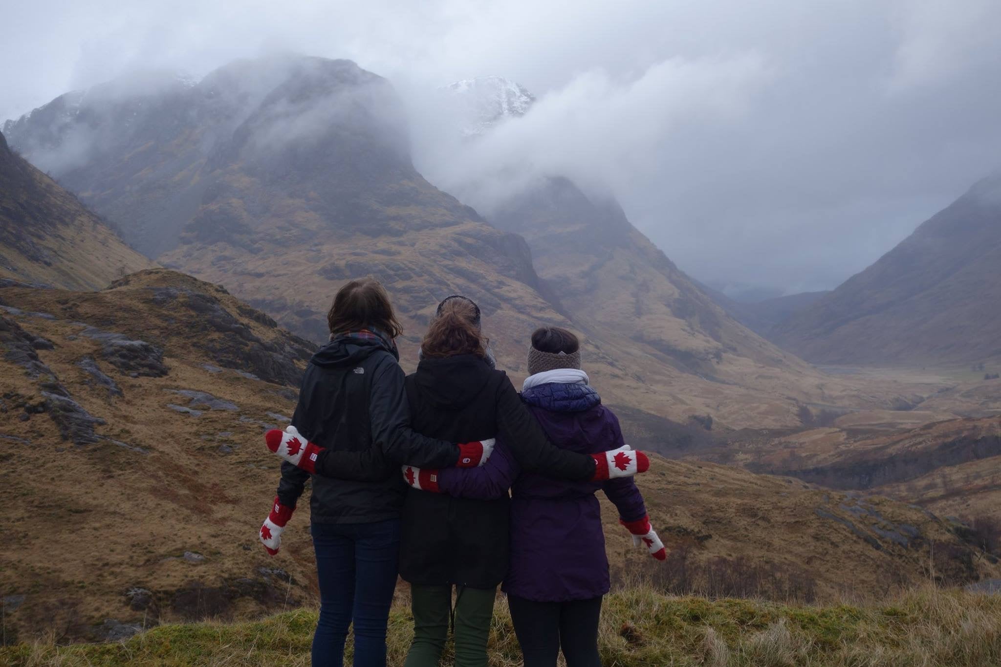Three girls standing in front of the Scotland highlands with Canadian flag mittens
