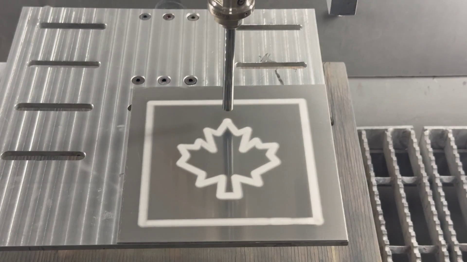 A nozzle above a finished Al2O3 cold spray deposition depicting a maple leaf.