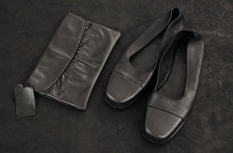 Pair of women's shoes and a clutch purse with a dark metallic finish sit on a concrete floor.