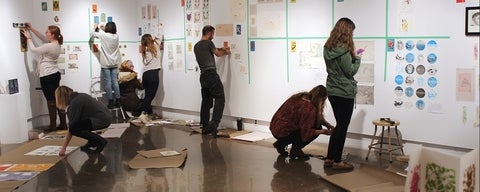 People installing artwork on gallery walls.