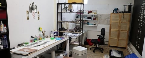 White-walled studio space with filled with small sculptures on a table, shelves and hanging on the walls. 