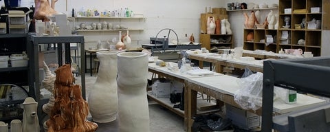 View of a ceramics studio with table and shelves filled with clay sculptures.