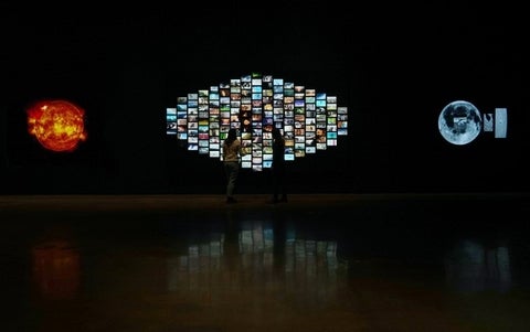 Two people standing in front of a digital video installation with 60 different videos.