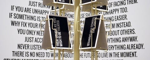 Artwork with text or euphemisms on a wall and a rotating postcard display stand with cards of euphemisms.