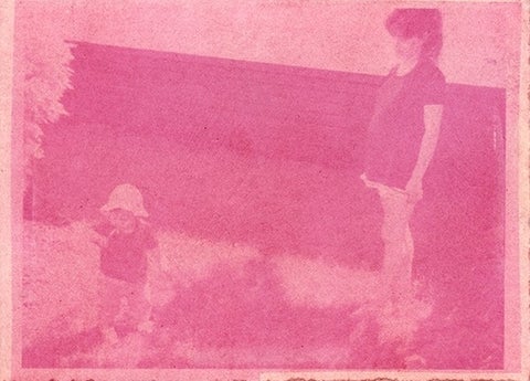 A blurred, bright pink image of a toddler and young women standing in the yard with a trailer wall behind them.