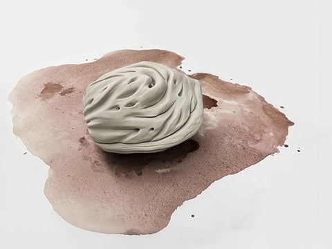 A large off-white porcelain peach pit rests atop an oxidized stain on a flat surface.