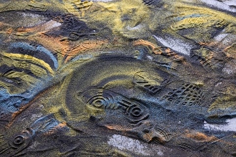 Artwork of swirls of artificially coloured sand disturbed by shoeprints.