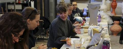 Art students seated at a table working on ceramic sculptures.