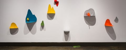 Artwork with multiple, colourful steel "shelves" holding small sculpture of rocks with legs.