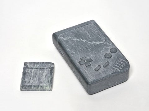 A pair of grey soapstone carvings reproduce a Ms. Pac-man cartridge sitting alongside a Nintendo Gameboy unit