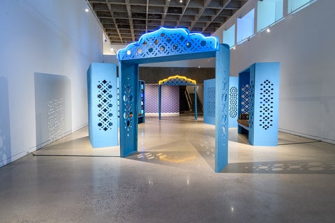 Art gallery with an installation of constructed wooden screen and seating areas painted blue and decorated with Islamic patterns.