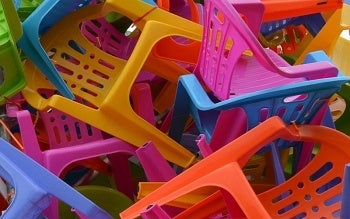 A close-cropped image of a mass of brightly coloured plastic chairs heaped together.