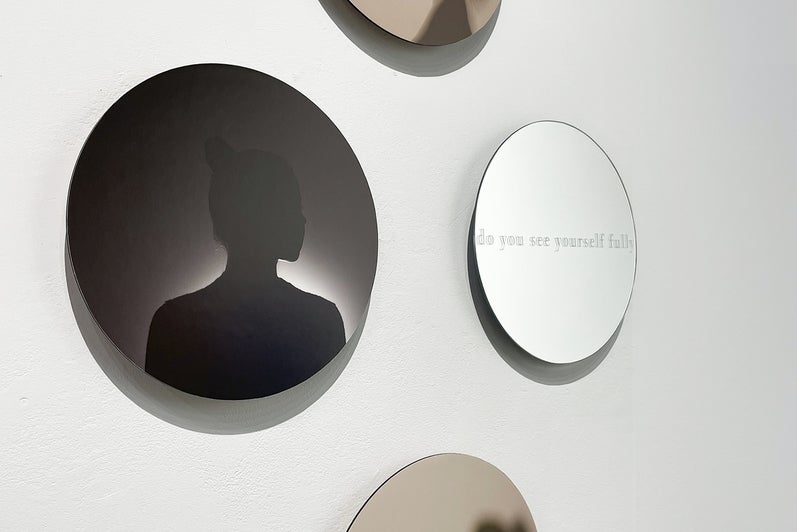 Art installation of 4 circular glass works with woman's portrait in silhouette and text "do you see yourself fully"