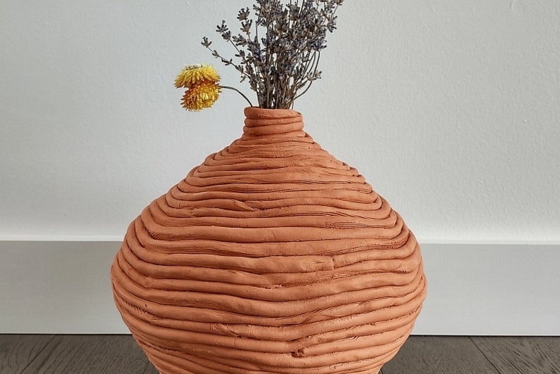 Coiled clay vessels containing dried flowers, sitting on the floor.