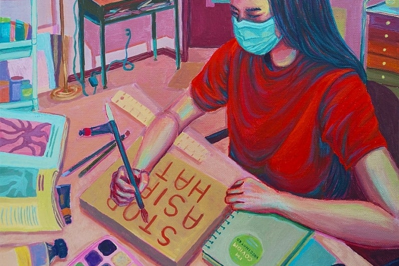 Painting of a girl wearing a face mask sits at a desk painting. Her canvas reads "Stop Asian Hate"