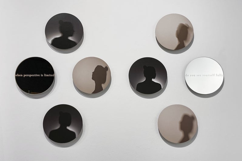 Art installation of 8 circular glass works. 6 show a woman's portrait in silhouette, 2 show text "when perspective is limited" a