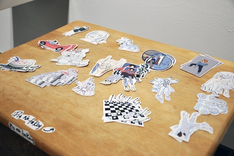 Detail of an art installation showing a folding table with stacks of anime-style stickers 