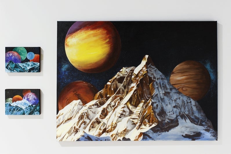 Art on gallery wall, three paintings of cosmic landscapes with icy mountains in front of multiple planets.