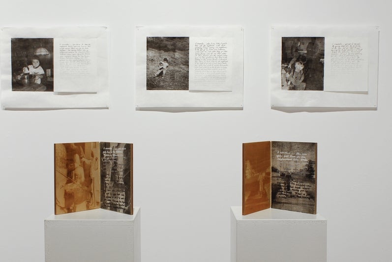 Installation in gallery of three black and white photos with accompanying text on the wall and two booklike, hinged, wooden pane