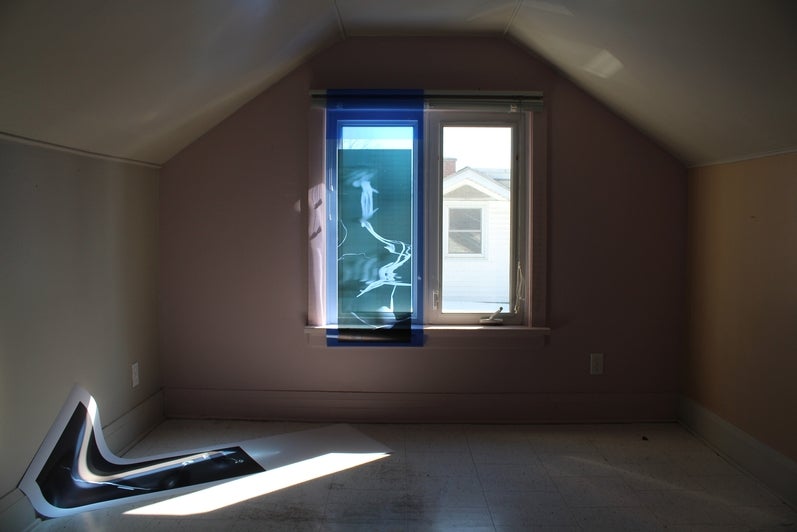 Empty room with light coming through window shining on paper picture on floor.  One window pane covered with transparent bluel