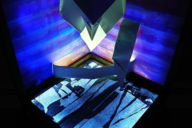 Viewed from above, a folded paper cobra hangs against a patterned blue background with a glowing lit abstract pattern underneath