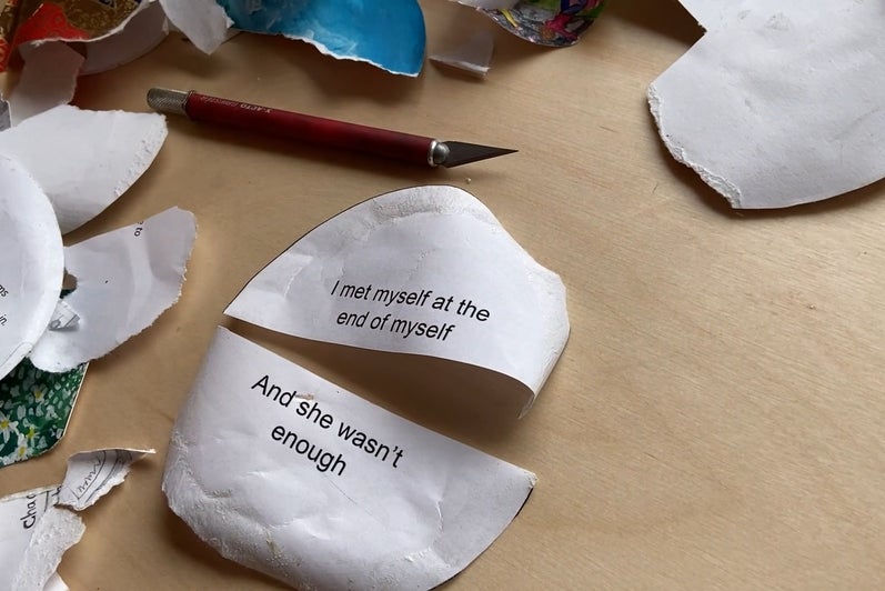 Table covered with bits of torn paper, a knife and a circular paper, cut in half, with text "I met myself at the end of myself a