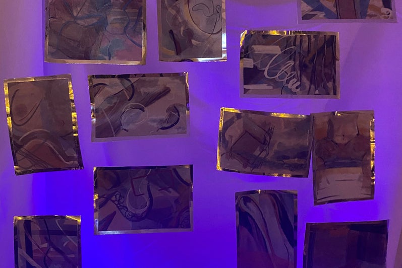 Purple and blue light on12 small abstract paintings hanging suspended.  Artworks edged with reflective material.