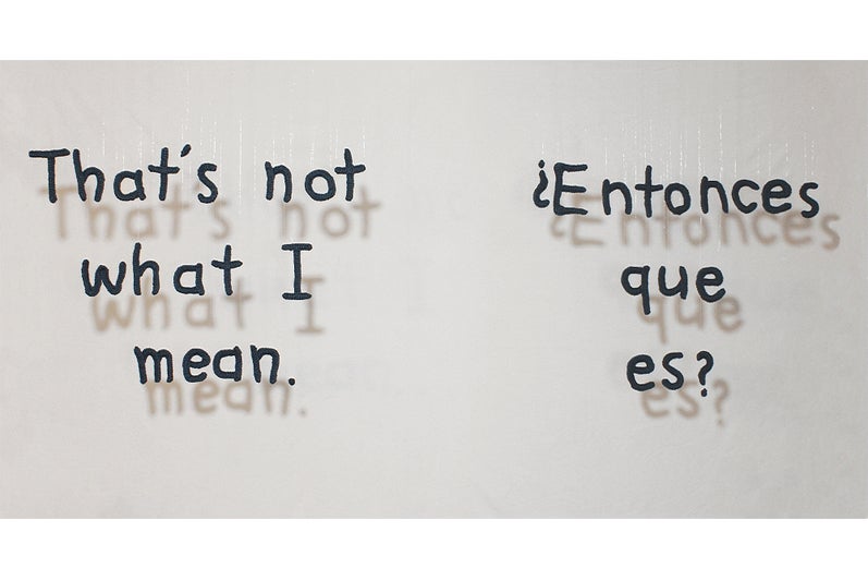 Hanging alphabetic letters cast a shadow on the wall behind.  Text reads "That's not what I mean. ¿Entonces que es? "