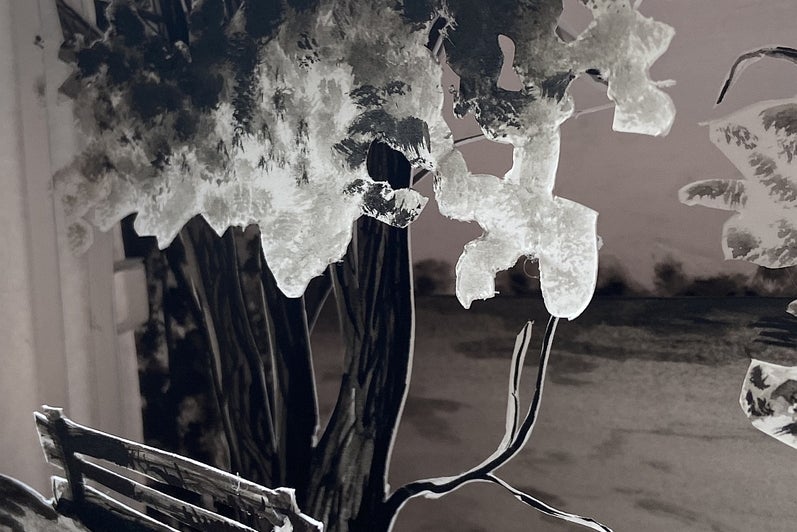 Shadow box made of paper layers showing a landscape with trees and a park bench in front.