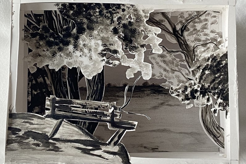 Shadow box made of paper layers showing a landscape with trees and a park bench in front.
