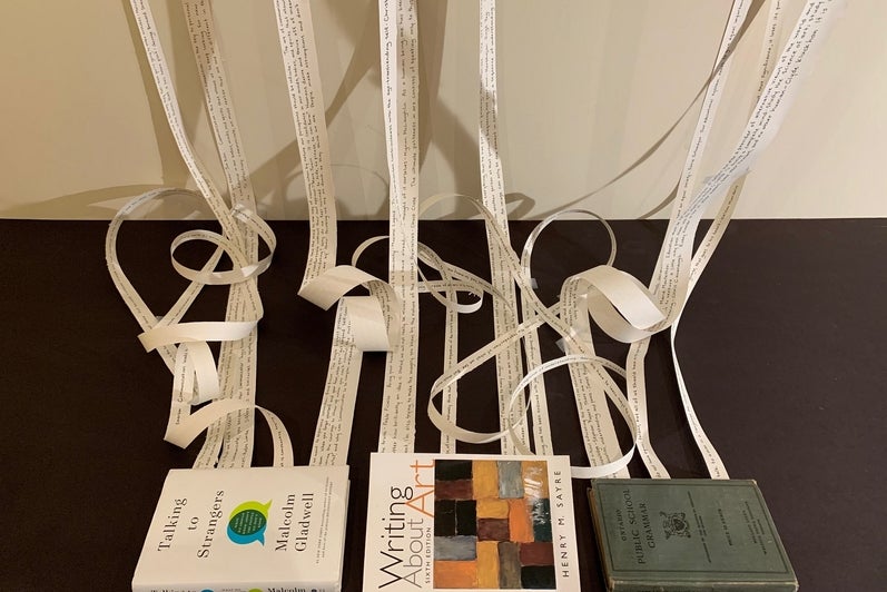 Art installation of three books lying on the floor with strips of paper coming from inside the books going up the wall