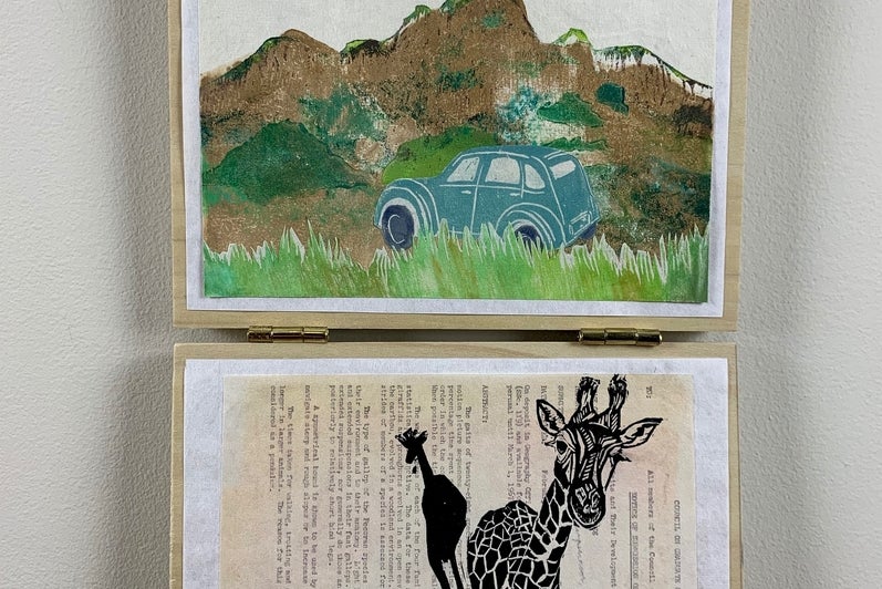 Two works of art hanging, top shows landscape is browns and green with a vintage blue car, lower two giraffes printed over text