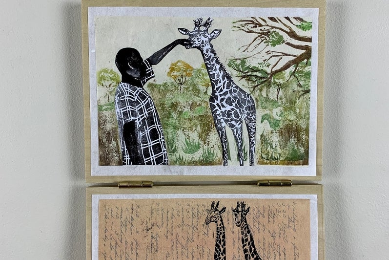 Two works of art hanging, top shows a figure reaching for a giraffe's head, lower two giraffes printed over text