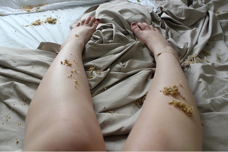Person's legs on rumpled sheet with bean sprouts scattered on top.