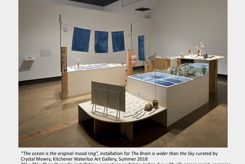 Art installation with tables of various heights display scientific-like objects and blue banners hanging above.