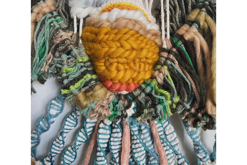 Wall hanging of patterned knotted yarn. Strips of blue and white hang from a yellow circle