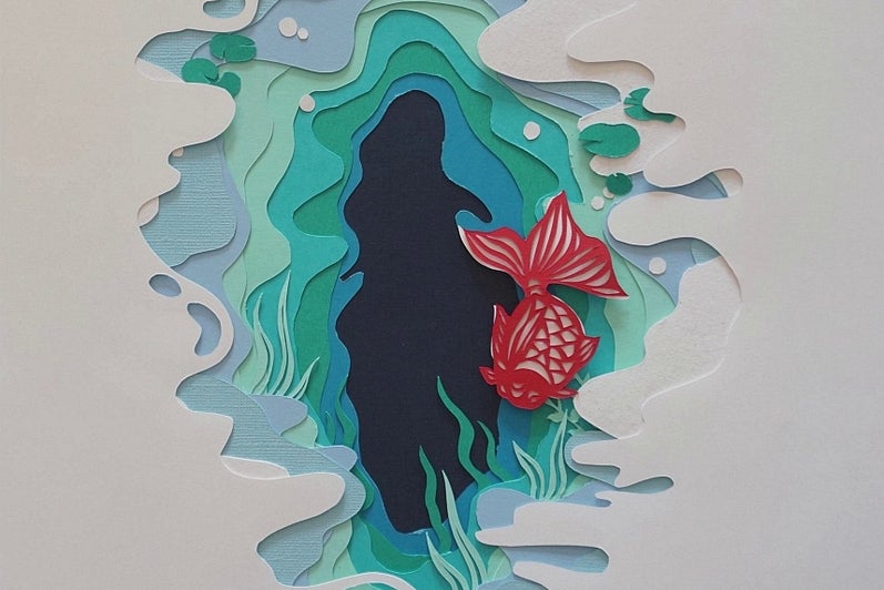 Paper cut-out artwork, white paper cut to reveal pages in shades of blue and green like water, orange carp swims.