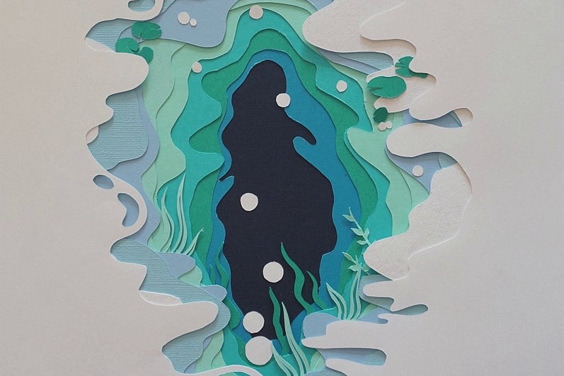 Paper cut-out artwork, white paper cut to reveal pages in shades of blue and green like water, small white circle like bubbles.